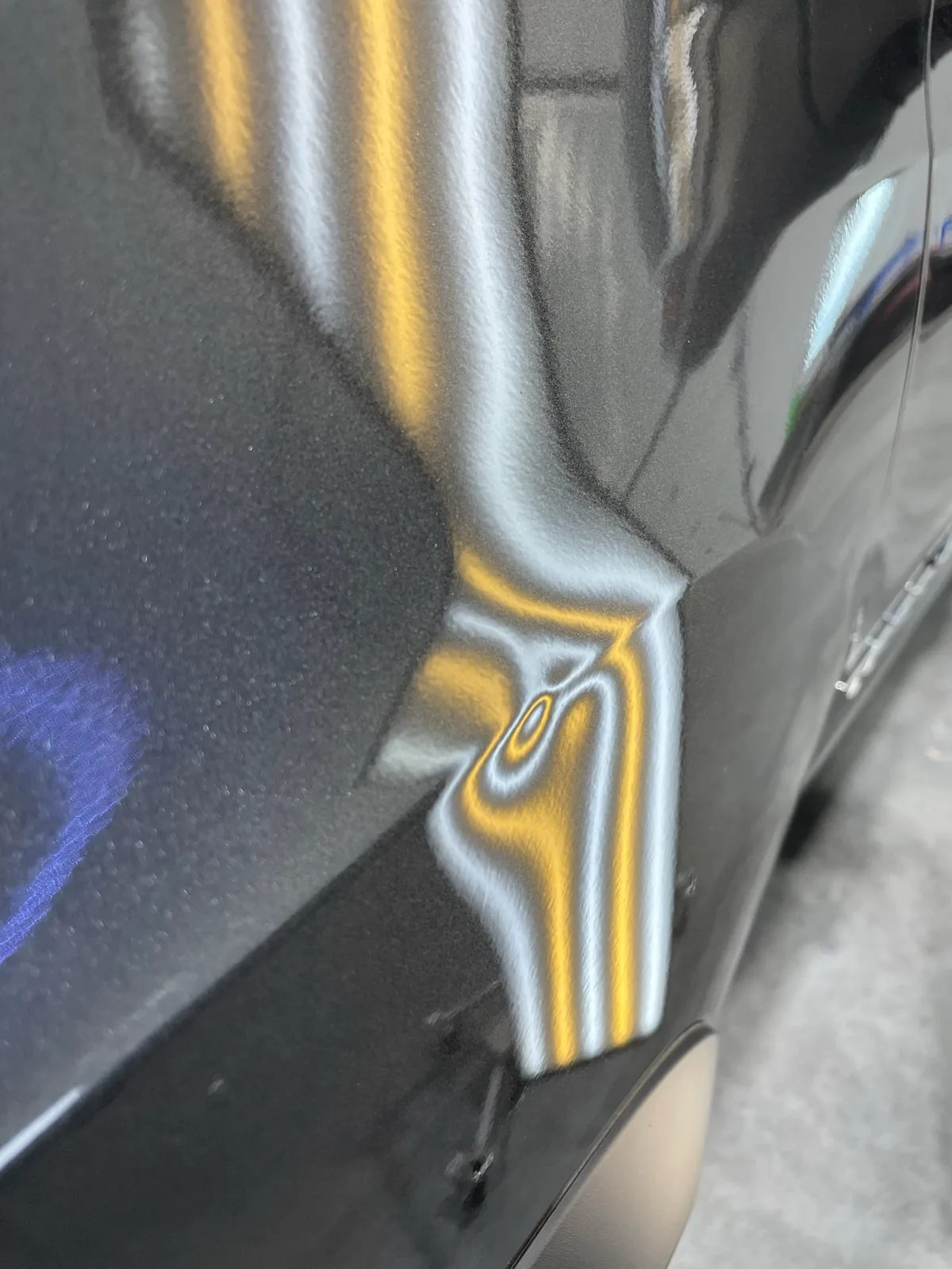 Black vehicle door panel with LED line-board revealing multiple hail dents along the body line