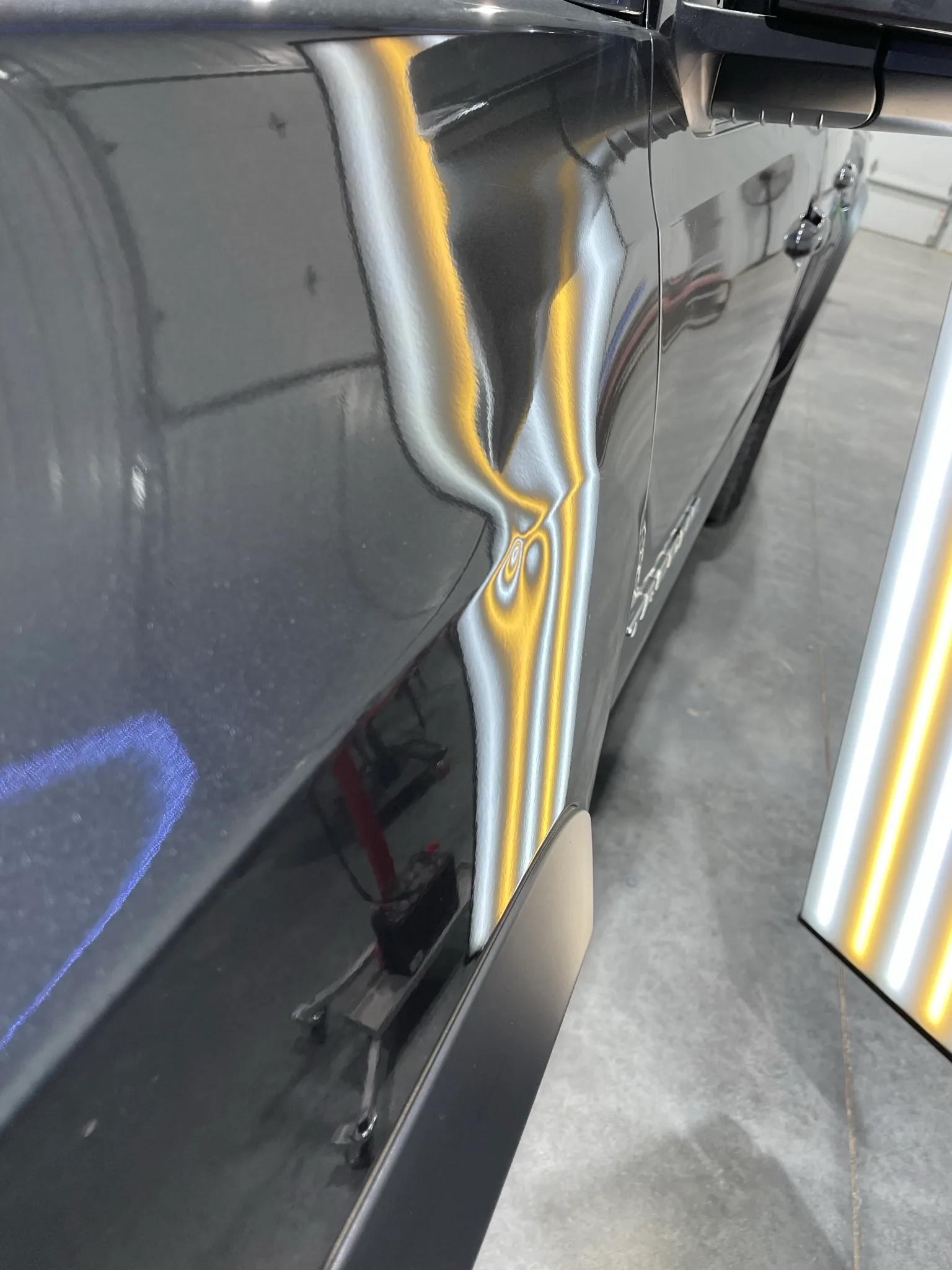 LED line board revealing hail dents on a dark hood before paintless dent repair at the Olathe shop