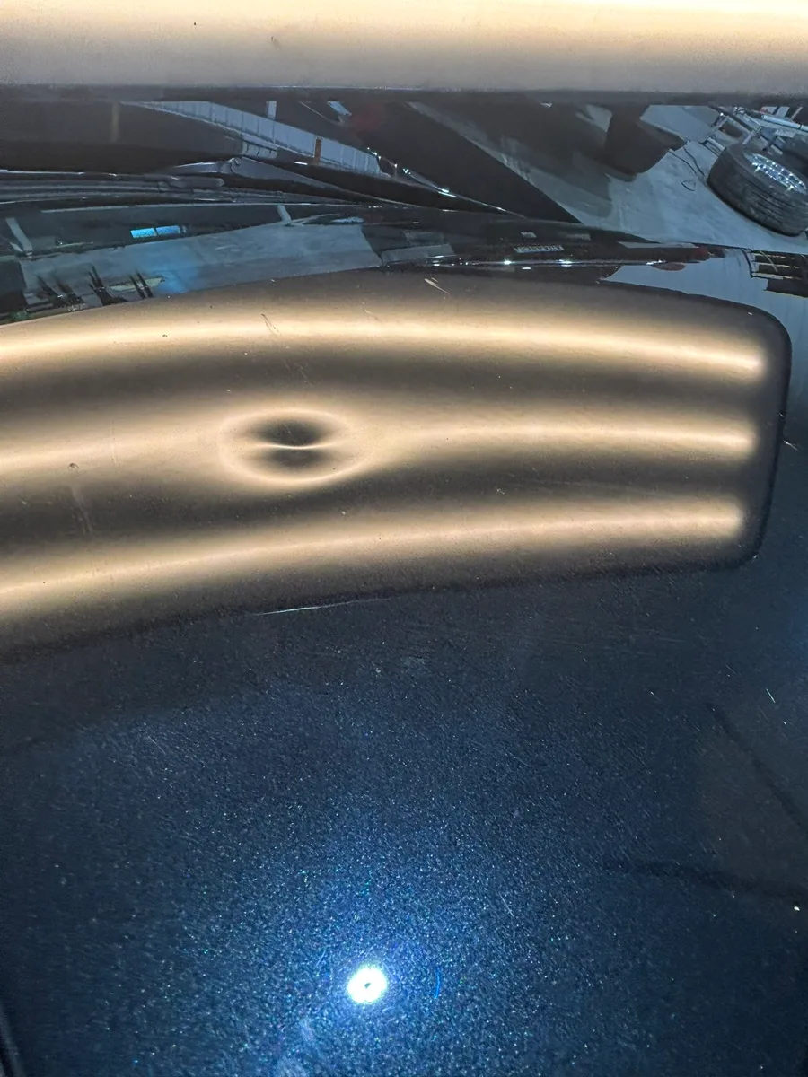 A hail dent on a vehicle hood under LED line-board inspection in Olathe, KS